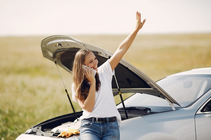 Mulher ao telefone ao lado de um automóvel com o capô aberto